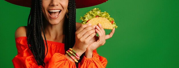 Close-up of happy young Mexican woman in Sombrero holding taco against green background - 749414333