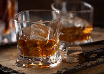 Glasses of whiskey with ice on rustic wooden tray