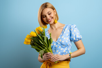 Joyful young woman holding bunch of tulips and smiling against blue background
