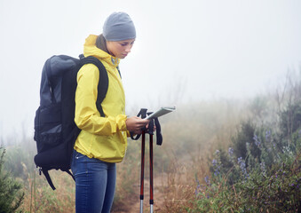 Woman, hiker and reading map on trail in nature, fog and guide for direction on mountain path. Sports gear in bag for supplies, adventure or fitness with natural winter for health in winter peace