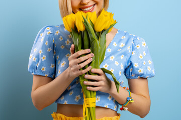 Close-up of young woman smelling fresh yellow tulips against blue background - 749420554