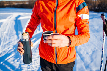 Person holding a cup of coffee and a thermos in the freezing snow