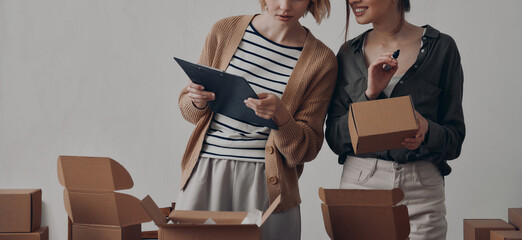 Two businesswomen preparing packages for delivery in warehouse together - 749422574