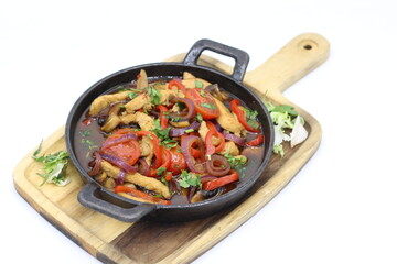 A sizzling pan filled with juicy meat and colorful vegetables rests on a wooden cutting board.