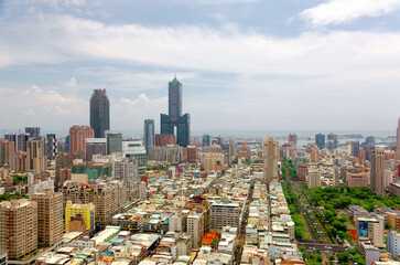 Naklejka premium Cityscape of Kaohsiung Downtown, a vibrant seaport city in Southern Taiwan, with the landmark 85 Sky Tower standing out among modern buildings and ships parking in the harbor under cloudy sunny sky