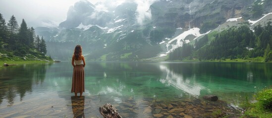 A woman in a long dress stands in a lake, gazing at the waters edge.