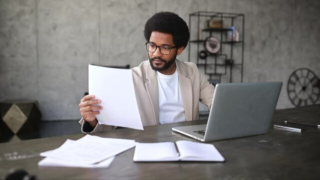 A focused businessman scrutinizes a document beside laptop, symbolizing in-depth analysis and attention to detail. This image captures the essence of diligent office work and decision-making processes