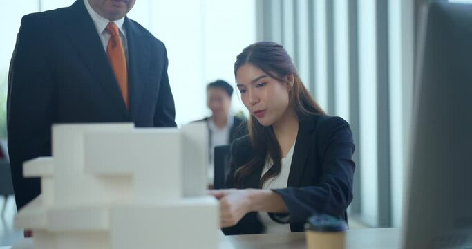 Asian business woman presenting building model with team in office. They dissing about building model design together.