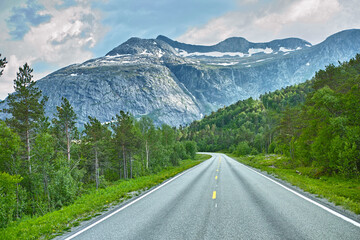 Mountain, road trip and forest highway with travel, holiday and countryside scenery in Norway. Nature, clouds in sky and street for journey, vacation and outdoor adventure with woods, trees and snow