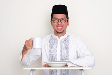 Moslem Asian man sitting on dinning table with one hand holding drinking glass