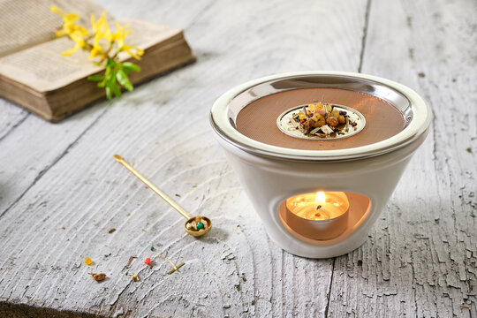 Burning incense (frankincense, resins and herbs) in an incense burner with tea light, spring  and easter still life on white wooden table