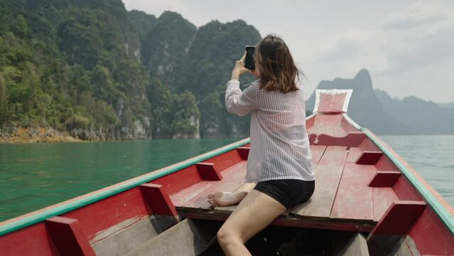 In a wooden boat a woman takes pictures of the lake