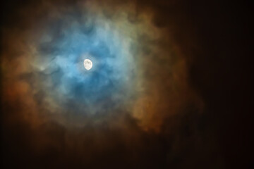 The Moon in the sky on a cloudy night is surrounded by colored clouds