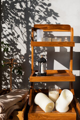 Wellness spa set for self care relaxation with a wooden shelf holding candles, glasses and a towel casting beautiful branches and leaves shadow on a white wall at home