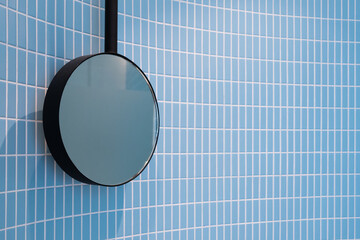 Minimalist round mirror black frame hang on a wall of ceramic baby blue tiles soft color embodying...