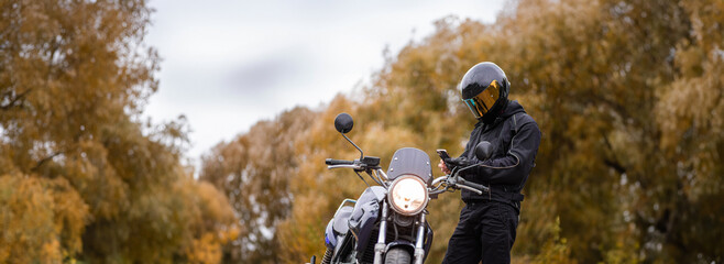 motorcyclist in a motorcycle jacket and tinted helmet with a classic motorcycle in nature. Stylish...