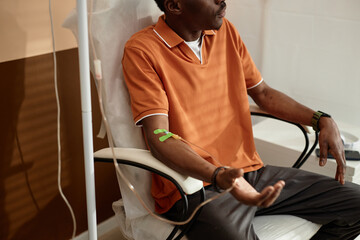 Cropped shot of Black adult man getting IV drip treatment in clinic sitting in chair with medical...