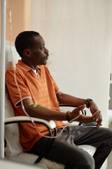 Vertical side view portrait of pensive African American man getting IV drip treatment sitting in...
