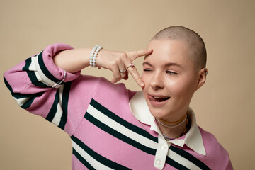 Portrait of gen Z young bald woman posing in studio against beige background and having fun