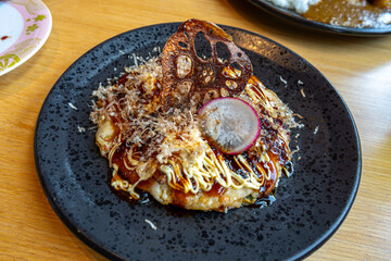 A delicate serving of a Japanese Okonomiyaki with various garnish on a black circular plate