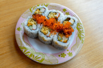 A serving of six sushi rice rolls with orange fish eggs garnish