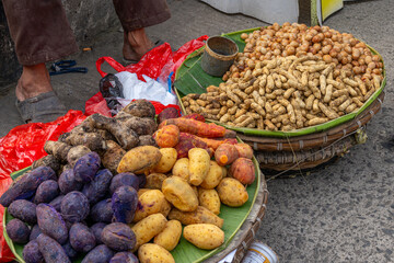 Two circular rattan bowls with a variety of boiled vegetables including sweet and purple potatoes, and peanuts