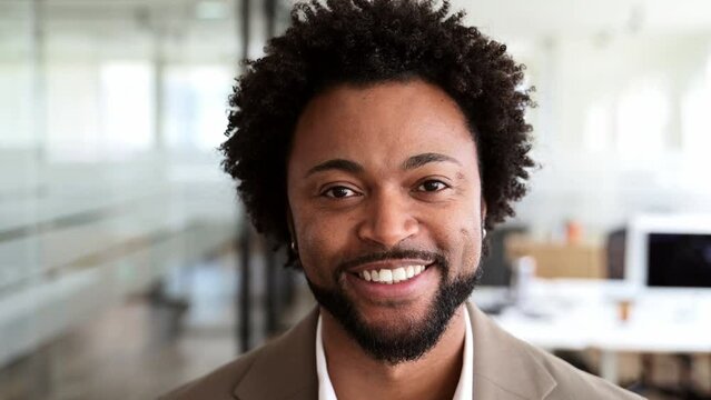 A close-up video portrait of a businessman in a light suit, capturing his confident smile and engaging personality in a contemporary office space, a sense of warmth and professional charisma
