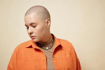 Obraz premium Minimal portrait of bald young woman wearing bright orange jacket looking away in studio, copy space