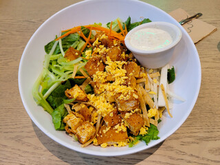 A delectable chicken salad served with a creamy dressing, artfully presented in a white bowl on a wooden table