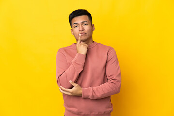 Young Ecuadorian man isolated on yellow background and thinking