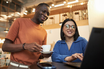 Waist up portrait of two smiling young people looking at laptop screen in coffee shop Black man and...