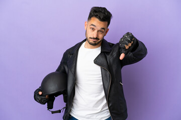 Young man with a motorcycle helmet isolated on purple background showing thumb down with negative expression