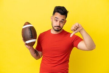 Young Caucasian man playing rugby isolated on yellow background showing thumb down with negative...