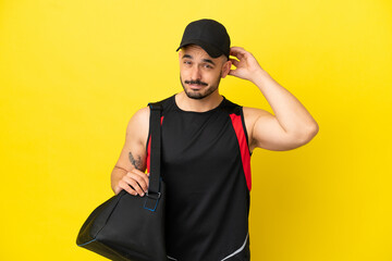 Young sport caucasian man with sport bag isolated on yellow background having doubts