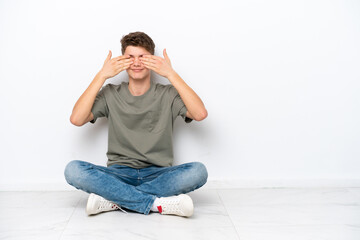 Teenager Russian man sitting on the floor isolated on white background covering eyes by hands