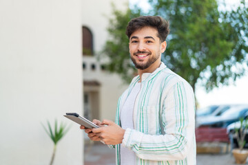 Handsome Arab man at outdoors holding a tablet with happy expression
