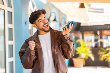 Handsome Arab man at outdoors using mobile phone and singing