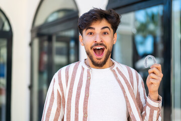 Handsome Arab man holding invisible braces at outdoors with surprise and shocked facial expression - obrazy, fototapety, plakaty