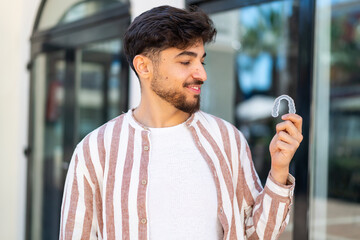 Handsome Arab man holding invisible braces at outdoors with happy expression