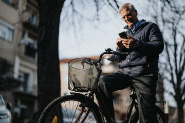 Mature businessman on bike checking smart phone in urban setting.