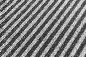 Striped shadow on gray asphalt. Shadow from iron railings on the sidewalk