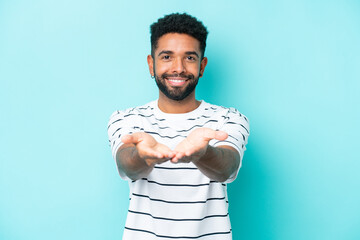 Young Brazilian man isolated on blue background holding copyspace imaginary on the palm to insert...
