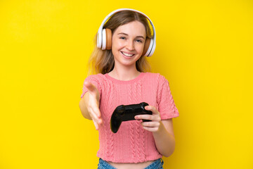 Blonde English young girl playing with a video game controller isolated on yellow background...
