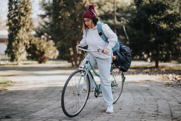 Focused young female with a beanie and glasses inspecting her bicycle tire outdoors on a chilly day, evoking a sense of independence.