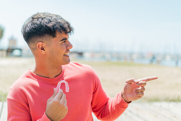 Young hispanic man holding invisible braces at outdoors pointing to the side to present a product