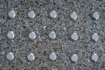 Stainless steel tactile ground surface indicators set in stone paving on walkway, closeup....