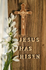 Jesus has risen text on wooden background, cross, white cloth and snowdrops
