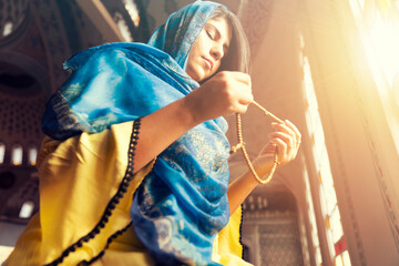 Muslim woman prays rosary. Muslim woman in traditional attire with hijab and rosary praying in a mosque - obrazy, fototapety, plakaty