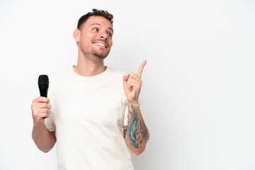 Young caucasian singer man picking up a microphone isolated on white background intending to...