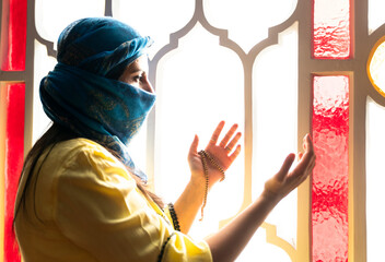 Muslim woman in headscarf and hijab prays with her hands up in air in mosque.Religion praying concept. 